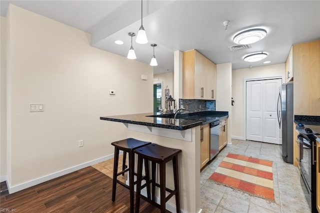 kitchen with kitchen peninsula, light brown cabinets, stainless steel appliances, and a kitchen breakfast bar