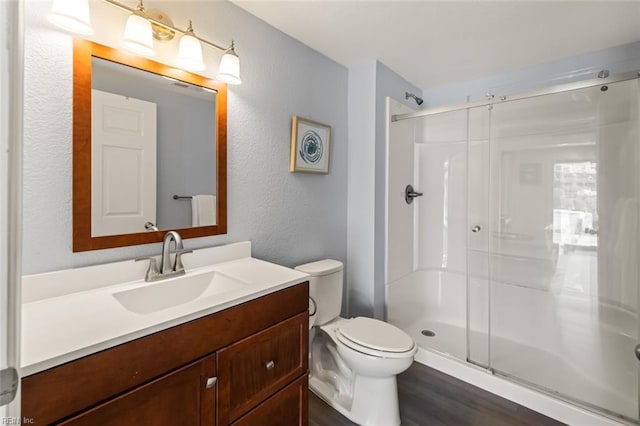 bathroom featuring a shower with door, vanity, hardwood / wood-style floors, and toilet