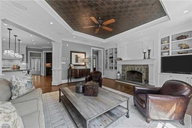 living room featuring light hardwood / wood-style floors, ornate columns, a tray ceiling, and built in features