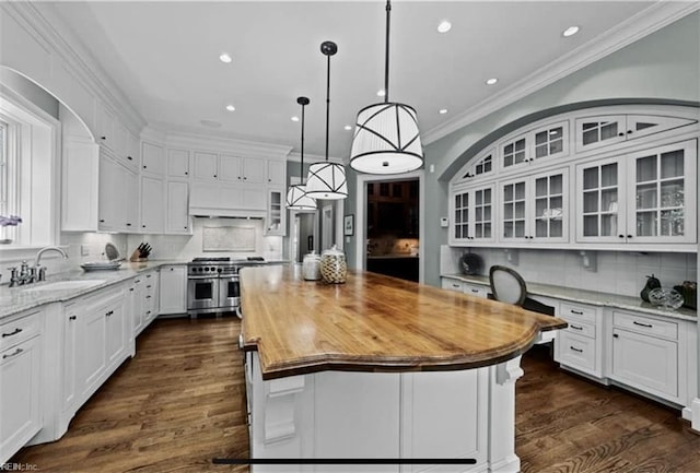 kitchen with sink, range with two ovens, white cabinets, a center island, and hanging light fixtures