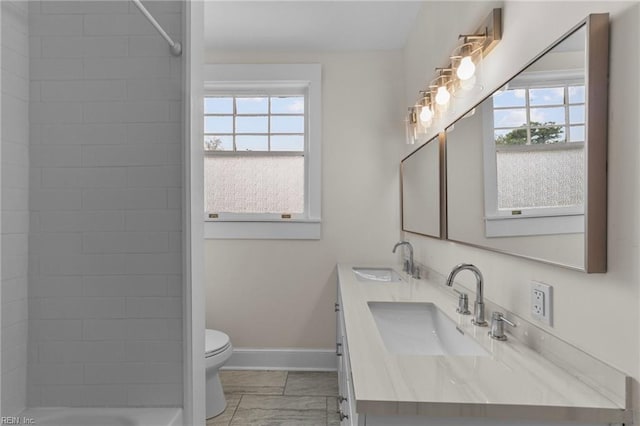 bathroom with a healthy amount of sunlight, oversized vanity, toilet, and double sink