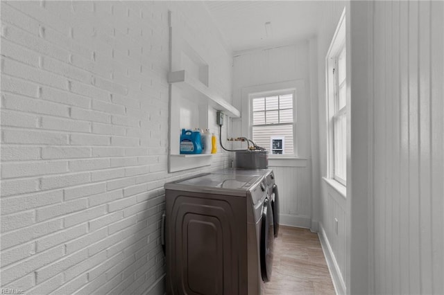 laundry room with brick wall, washer and clothes dryer, and light hardwood / wood-style floors