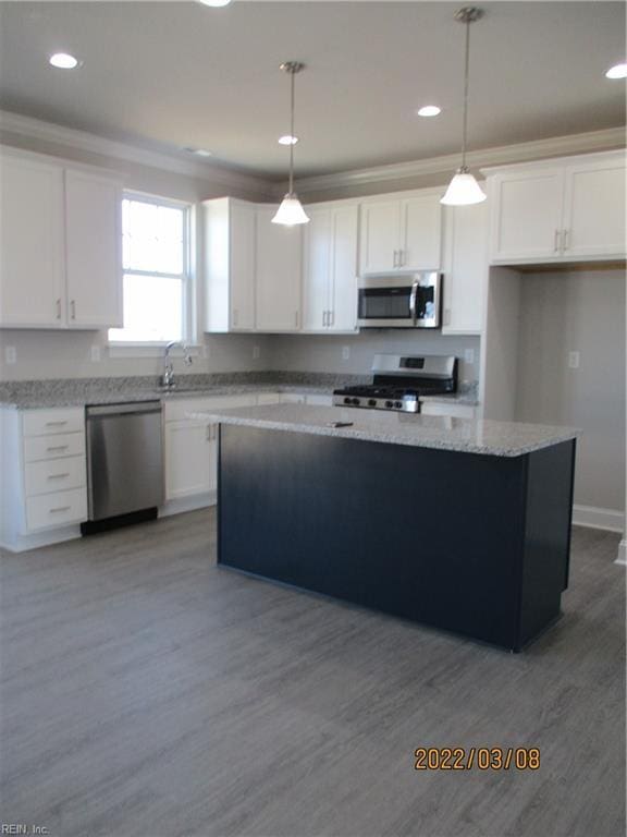 kitchen featuring white cabinetry, hanging light fixtures, stainless steel appliances, light stone countertops, and a kitchen island