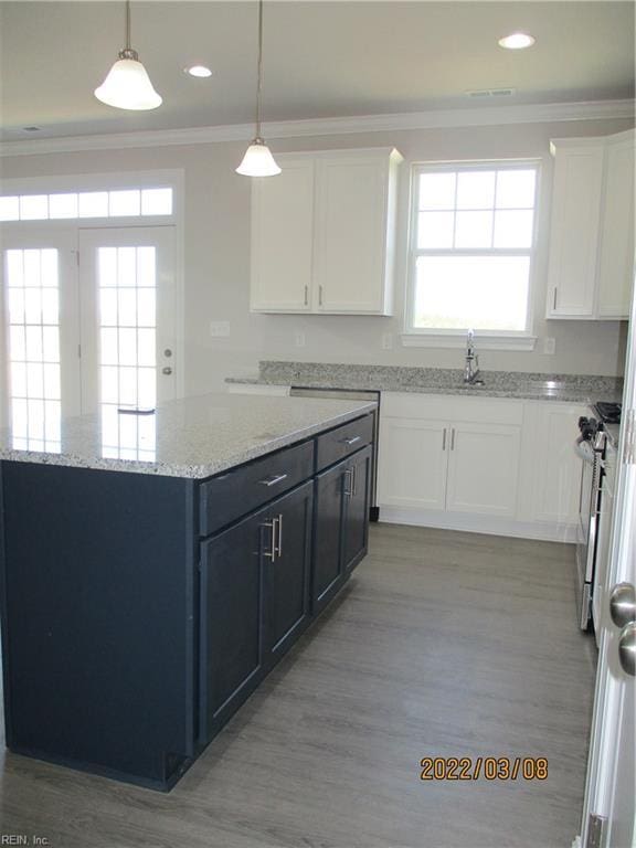 kitchen featuring pendant lighting, stainless steel gas stove, white cabinetry, ornamental molding, and light stone counters