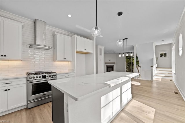 kitchen featuring light stone countertops, a center island, wall chimney exhaust hood, white cabinetry, and stainless steel range with gas stovetop