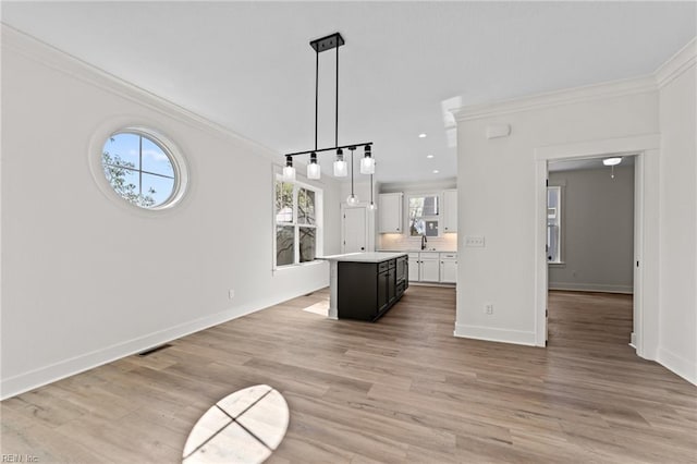 kitchen with light hardwood / wood-style floors, pendant lighting, crown molding, white cabinets, and a center island