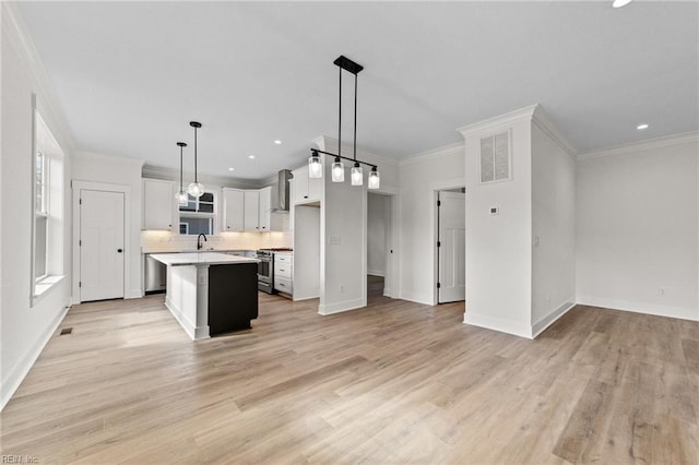 kitchen with a center island, wall chimney exhaust hood, hanging light fixtures, crown molding, and stainless steel range with gas stovetop