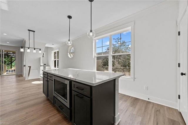 kitchen with stainless steel microwave, light wood-type flooring, pendant lighting, and a kitchen island