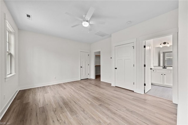 unfurnished bedroom with ensuite bathroom, ceiling fan, light wood-type flooring, and multiple windows