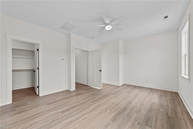 unfurnished bedroom featuring ceiling fan, a closet, a walk in closet, light hardwood / wood-style flooring, and multiple windows