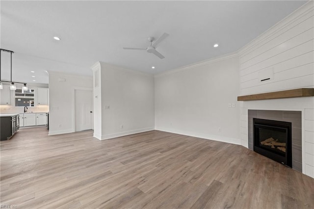 unfurnished living room featuring ceiling fan, light hardwood / wood-style flooring, ornamental molding, and a fireplace