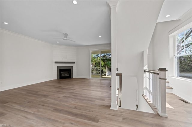 unfurnished living room featuring ceiling fan, a large fireplace, crown molding, and light hardwood / wood-style flooring