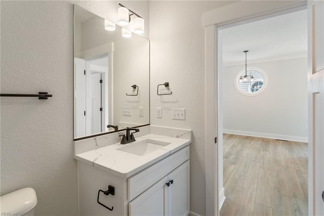 bathroom featuring toilet, vanity, wood-type flooring, an inviting chandelier, and ornamental molding