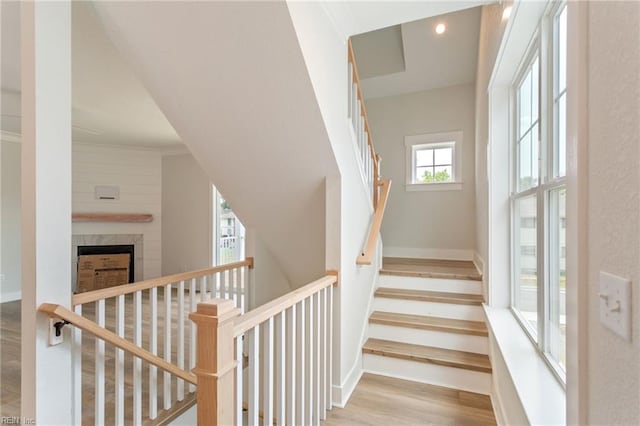 stairs featuring wood-type flooring, a tile fireplace, and crown molding