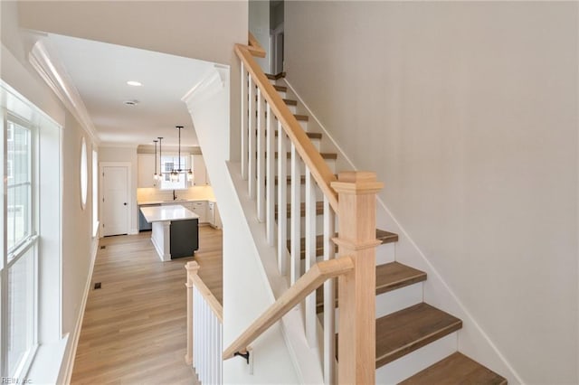 staircase with ornamental molding, a chandelier, hardwood / wood-style floors, and sink