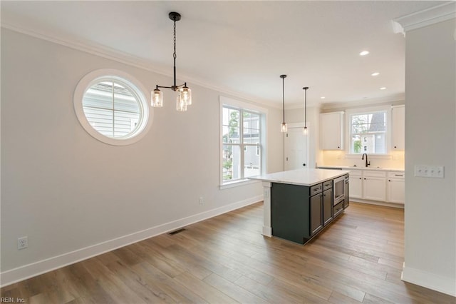 kitchen featuring decorative light fixtures, a kitchen island, wood-type flooring, crown molding, and white cabinetry