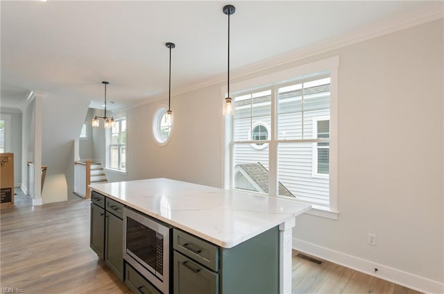 kitchen with stainless steel microwave, a kitchen island, decorative light fixtures, ornamental molding, and light stone counters