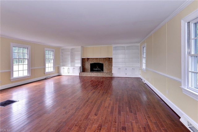 unfurnished living room featuring built in shelves, dark wood-type flooring, crown molding, and a tiled fireplace