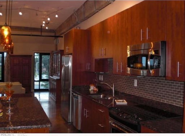 kitchen featuring decorative backsplash, appliances with stainless steel finishes, dark stone counters, sink, and pendant lighting