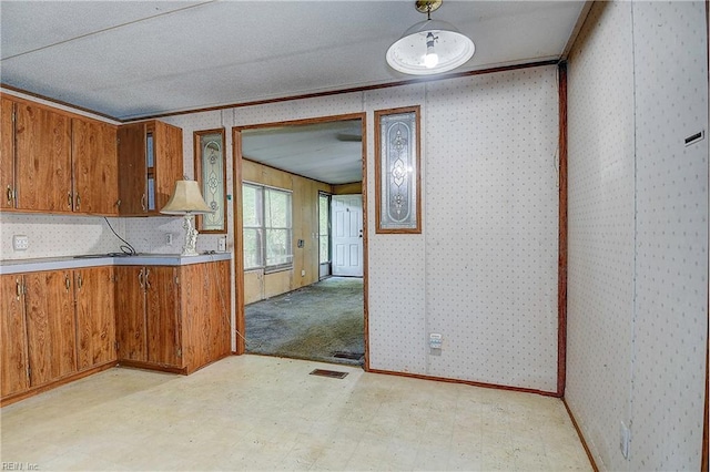 kitchen with wallpapered walls, brown cabinetry, light floors, and light countertops