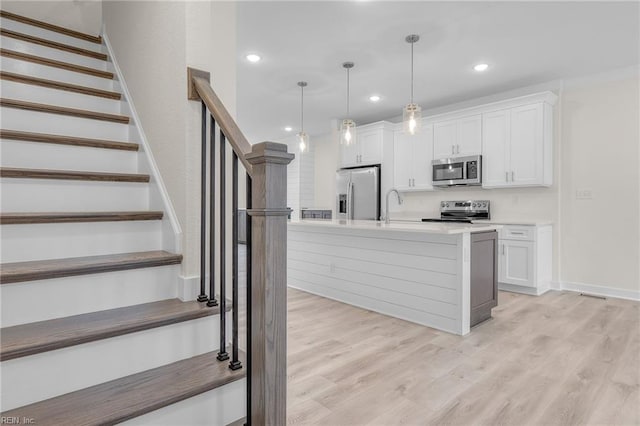 kitchen featuring pendant lighting, stainless steel appliances, a kitchen island with sink, and white cabinets