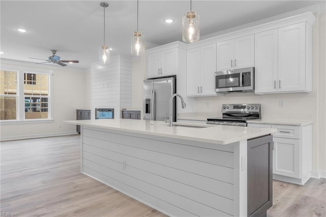 kitchen featuring sink, stainless steel appliances, an island with sink, white cabinets, and decorative light fixtures