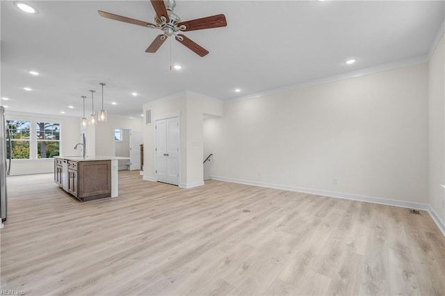 unfurnished living room featuring crown molding, ceiling fan, sink, and light hardwood / wood-style floors