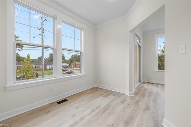 unfurnished room featuring ornamental molding, a healthy amount of sunlight, an inviting chandelier, and light hardwood / wood-style floors