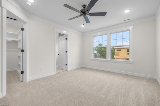 unfurnished bedroom featuring a spacious closet, light colored carpet, ornamental molding, a closet, and ceiling fan