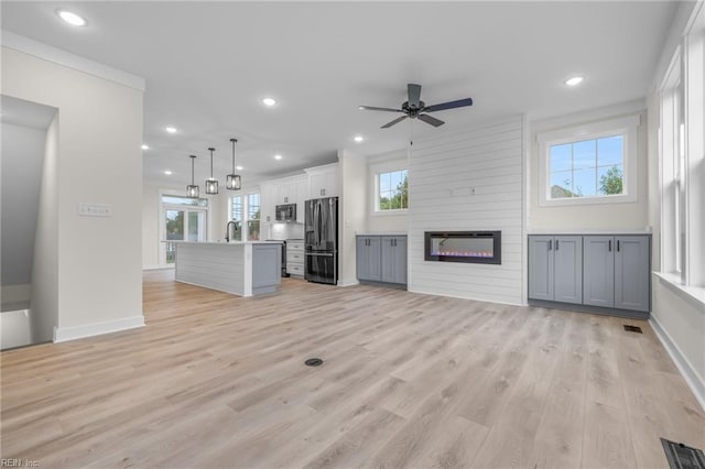 unfurnished living room featuring sink, a large fireplace, ceiling fan, crown molding, and light wood-type flooring