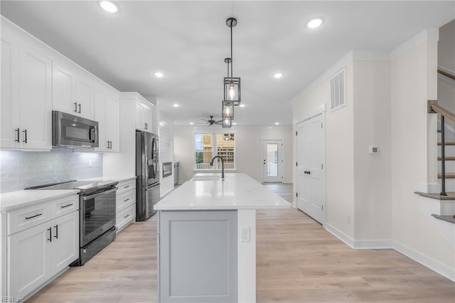 kitchen featuring appliances with stainless steel finishes, white cabinetry, hanging light fixtures, backsplash, and a center island with sink