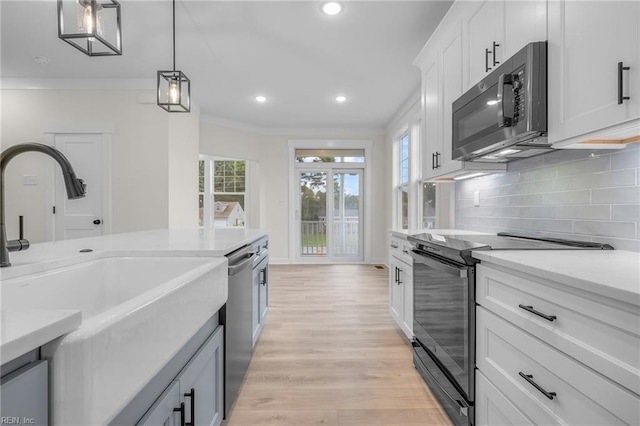 kitchen with sink, appliances with stainless steel finishes, ornamental molding, white cabinets, and decorative light fixtures