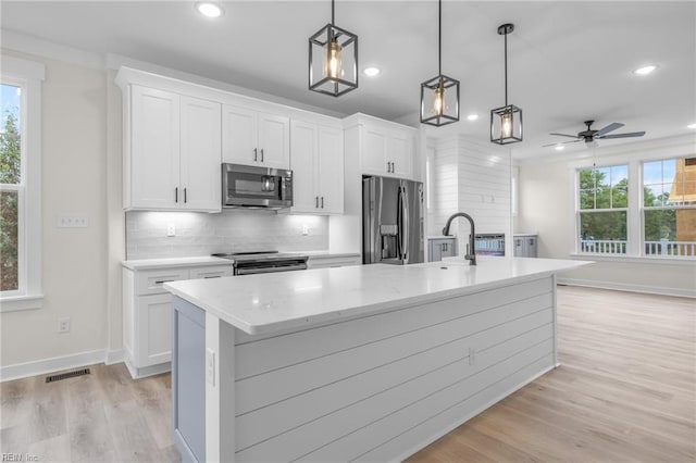 kitchen with pendant lighting, stainless steel appliances, tasteful backsplash, an island with sink, and white cabinets