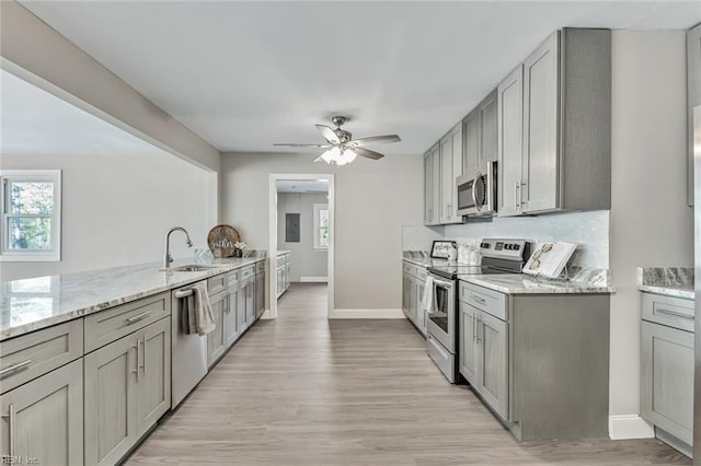 kitchen with appliances with stainless steel finishes, gray cabinets, light stone counters, and sink