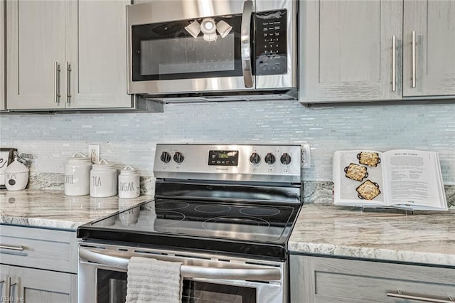 kitchen with gray cabinetry, light stone countertops, appliances with stainless steel finishes, and tasteful backsplash