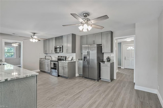 kitchen with stainless steel appliances, light stone counters, gray cabinets, decorative backsplash, and light wood-type flooring