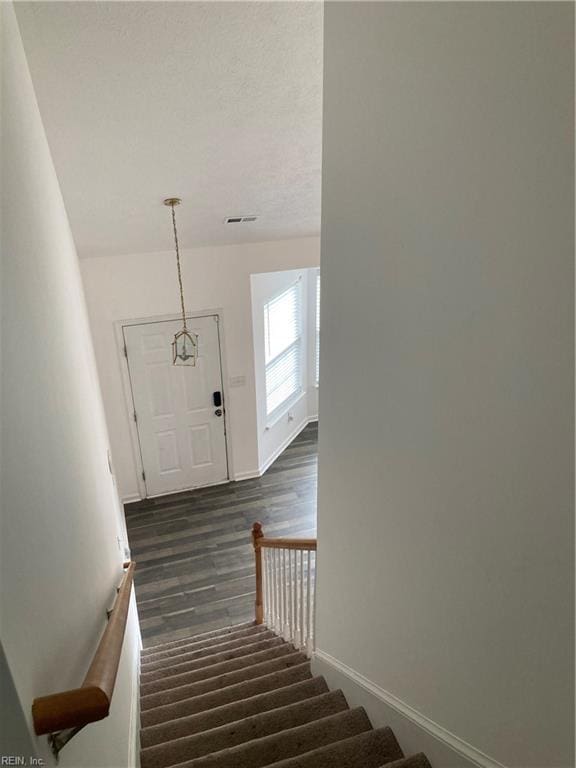 stairs featuring wood-type flooring and an inviting chandelier