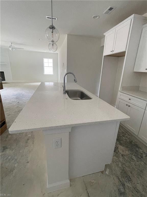 kitchen featuring white cabinetry, sink, an island with sink, and light stone counters