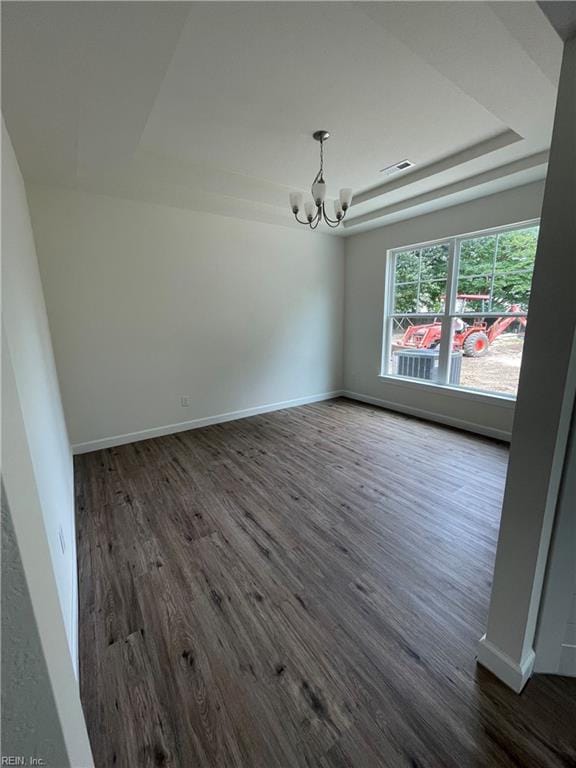 empty room with a tray ceiling, dark hardwood / wood-style floors, and a notable chandelier