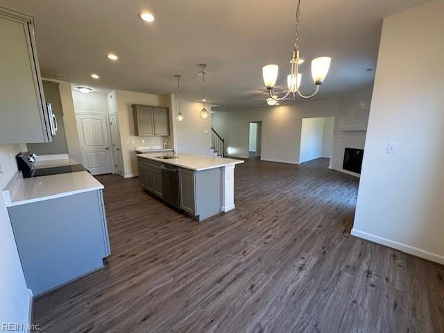 kitchen with pendant lighting, dark wood-type flooring, a center island with sink, stainless steel dishwasher, and a large fireplace