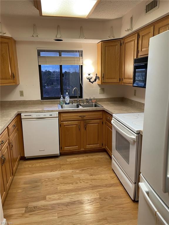 kitchen with a textured ceiling, white appliances, light hardwood / wood-style floors, and sink