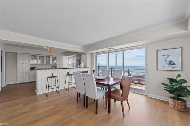 dining area featuring light hardwood / wood-style floors, ornamental molding, and a water view