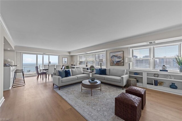 living room with built in features, light hardwood / wood-style flooring, a water view, and crown molding