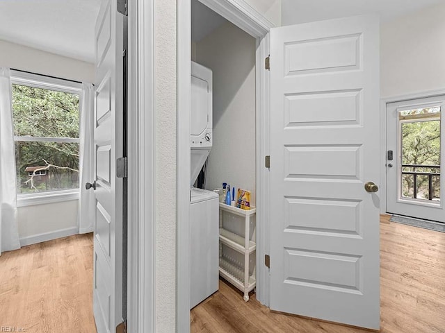 laundry room featuring stacked washing maching and dryer and light hardwood / wood-style floors