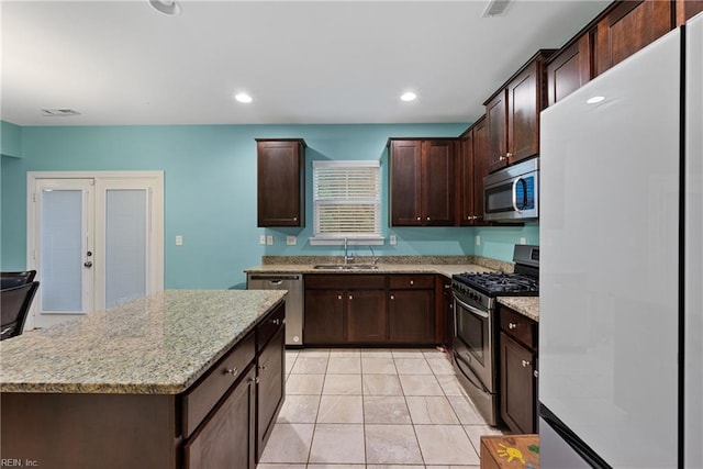 kitchen with appliances with stainless steel finishes, sink, dark brown cabinetry, light stone countertops, and light tile patterned flooring