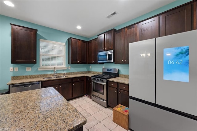 kitchen featuring stainless steel appliances, sink, light stone counters, a wealth of natural light, and light tile patterned floors