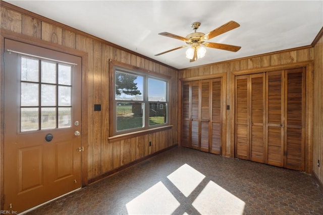 doorway with crown molding, ceiling fan, and wooden walls