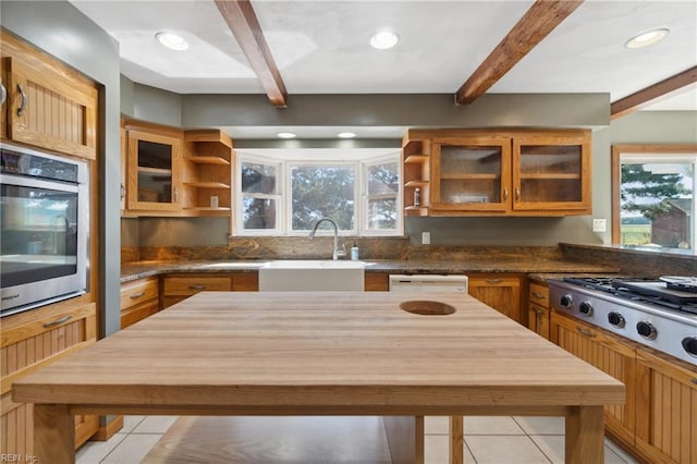 kitchen featuring sink, light tile patterned floors, appliances with stainless steel finishes, and beam ceiling