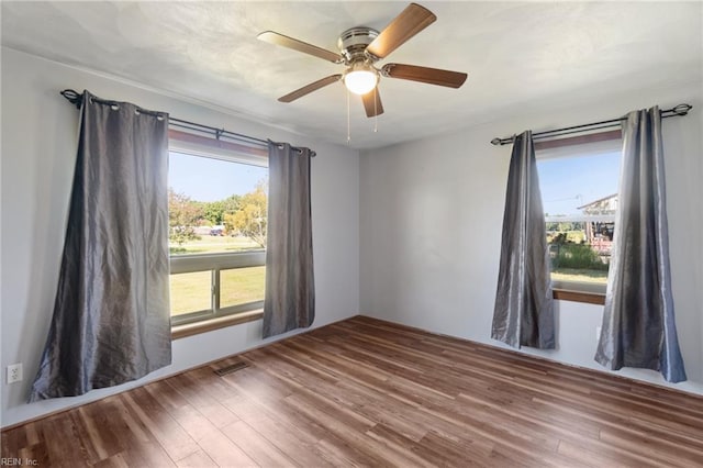 empty room featuring ceiling fan, plenty of natural light, and wood-type flooring