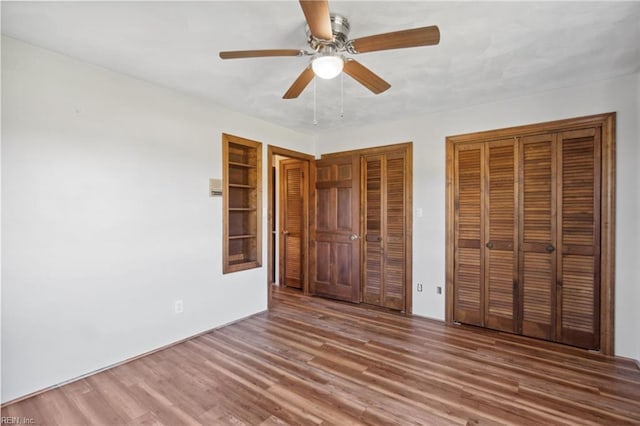 unfurnished bedroom with ceiling fan, two closets, and dark hardwood / wood-style flooring